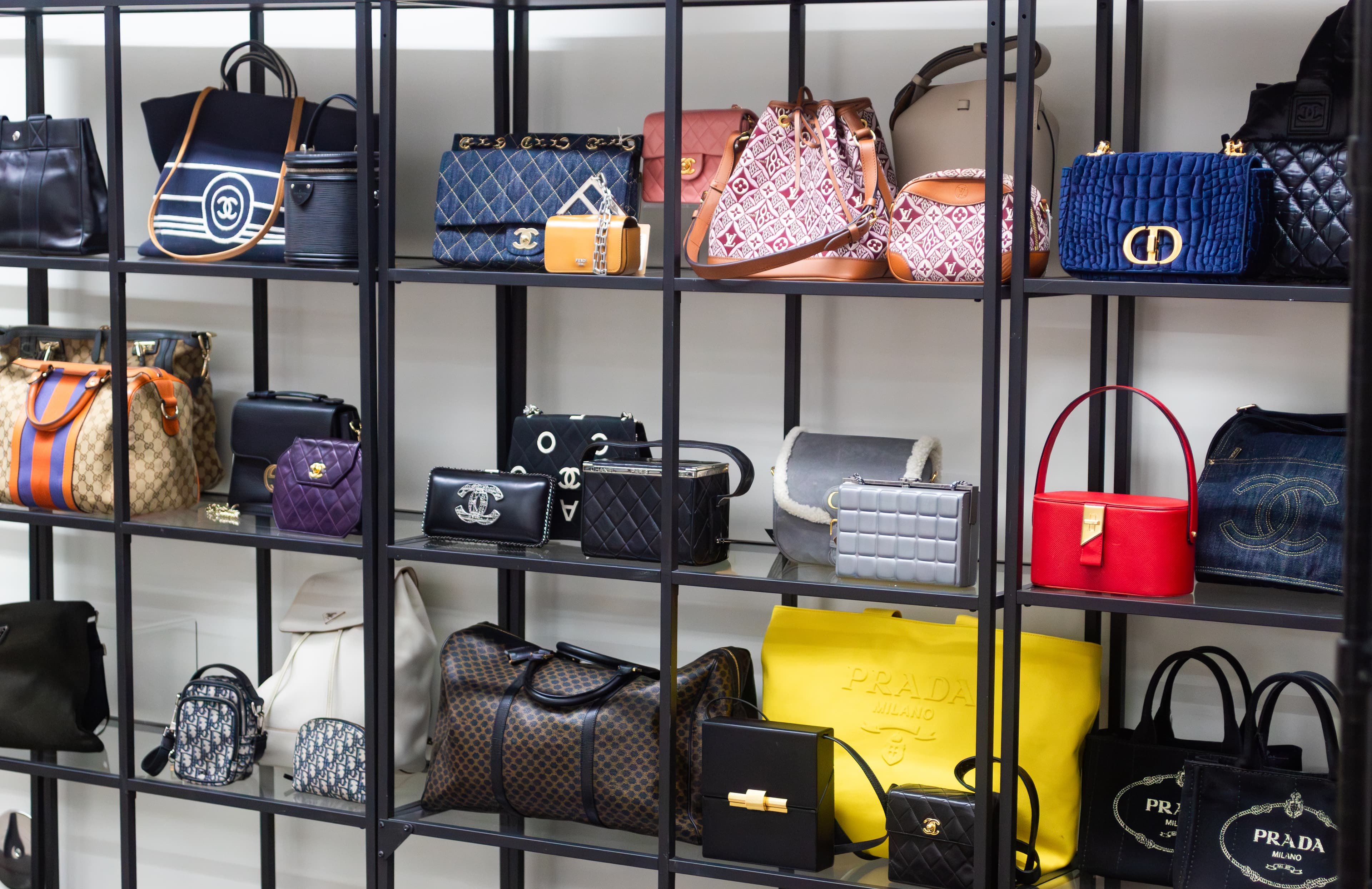 Luxury handbags displayed on black shelves, featuring quilted, leather, and patterned designs in various colors and styles.