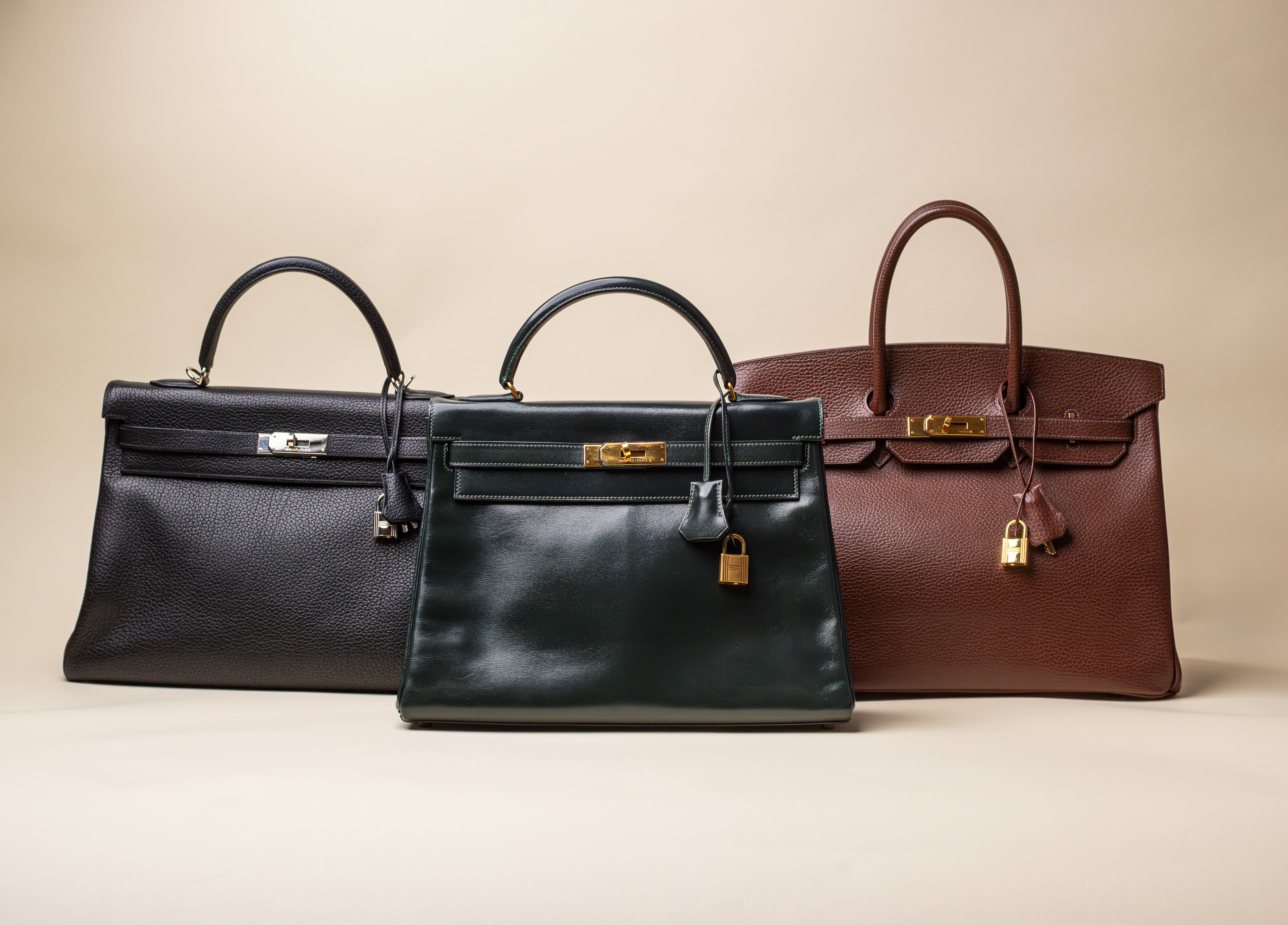 Three leather handbags in black, dark green, and brown with gold locks on a beige background.